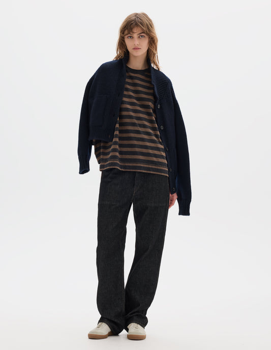 Full body image, front view of model wearing a dark navy blue boxy fit collared cardigan, with laid-on side entry pockets, and rib detailing on collar, placket, hem and cuffs. Worn open, styled with a striped brown and black jersey top, black denim trousers and off white suede trainers.