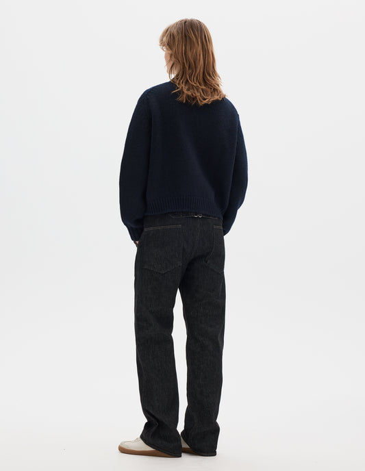Full body image, back view of model wearing a dark navy blue boxy fit collared cardigan, rib detailing on hem and cuffs. Styled with black denim trousers and off white suede trainers.