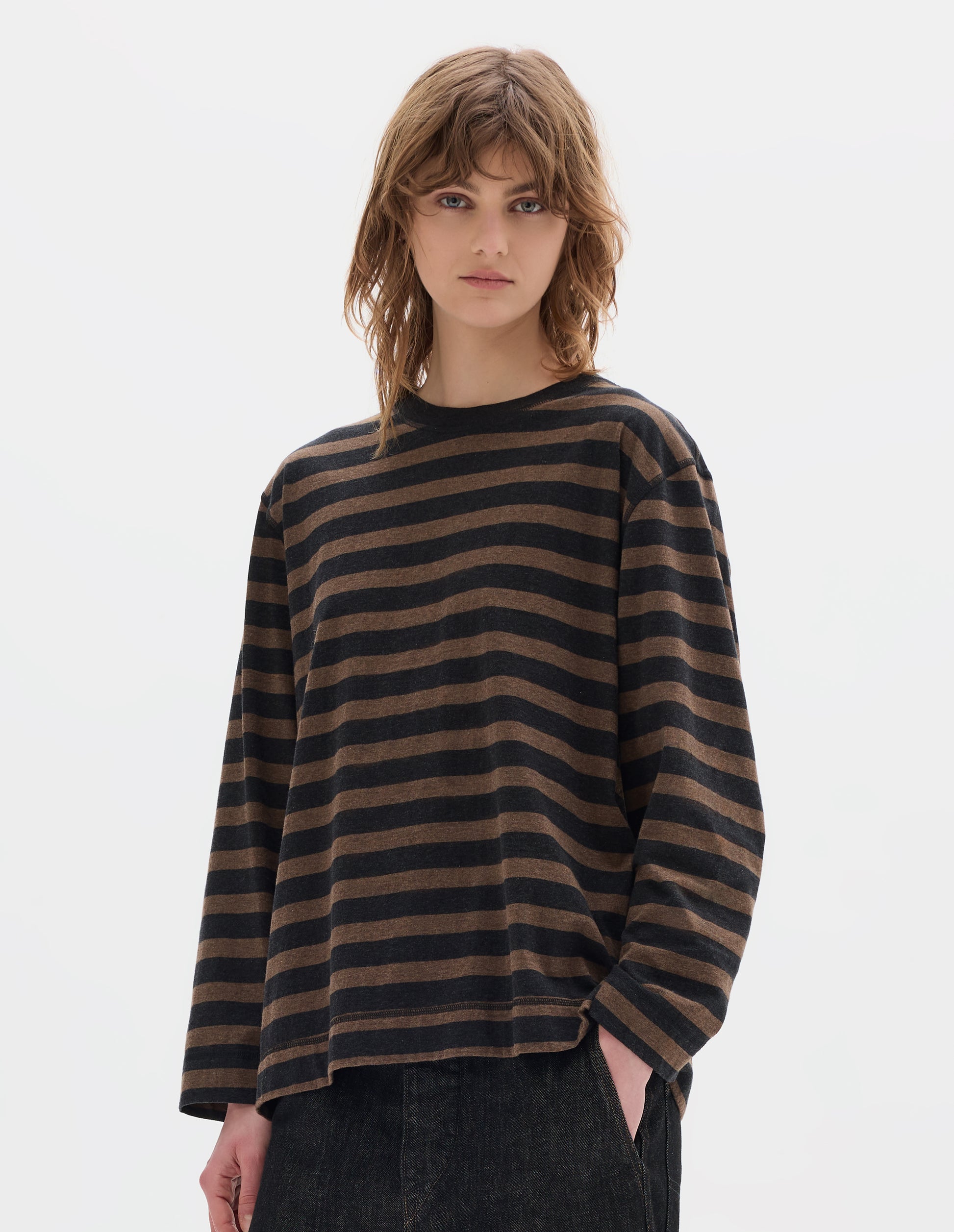 Cropped body image, front view of model wearing off black and brown stripe cotton top, with contrasting rib neck and flatlock stitch detailing on the seams. Styled with black jeans.