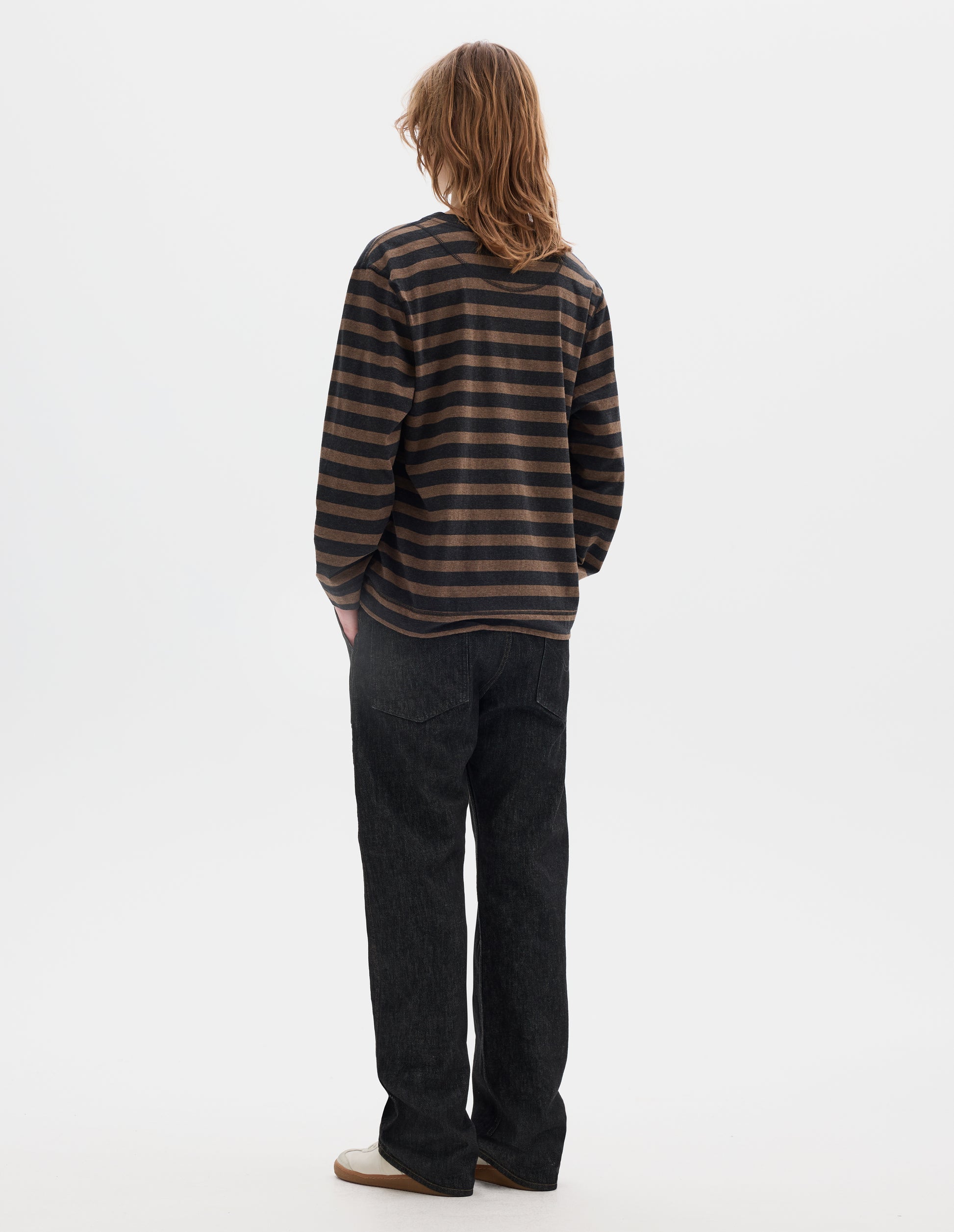 Full body image, back view of model wearing off black and brown stripe cotton top, with contrasting rib neck and flatlock stitch detailing on the seams. Styled with black jeans and white shoes.