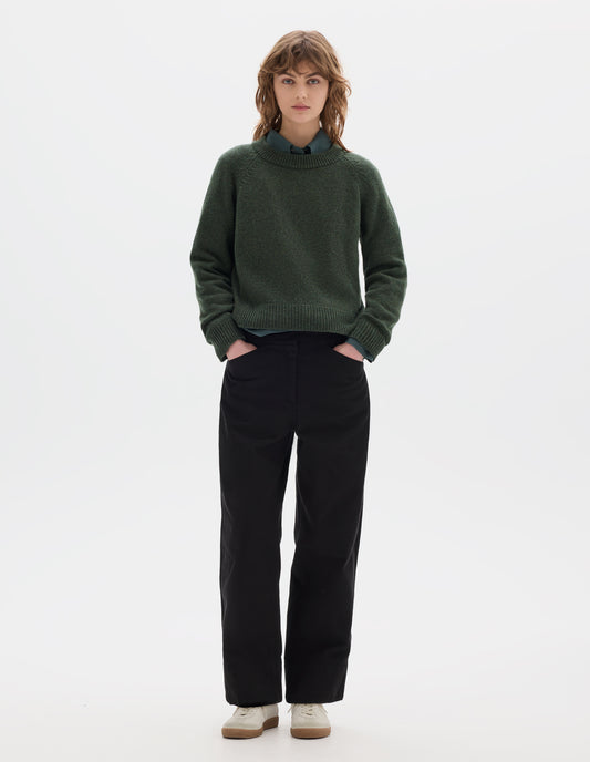 Full body image, front view of model wearing green knitted wool jumper with crew neck, raglan sleeves, and rib detailing on the neck, cuffs and hem. Styled over green cotton shirt, with black cotton trousers and white trainers with gum sole.