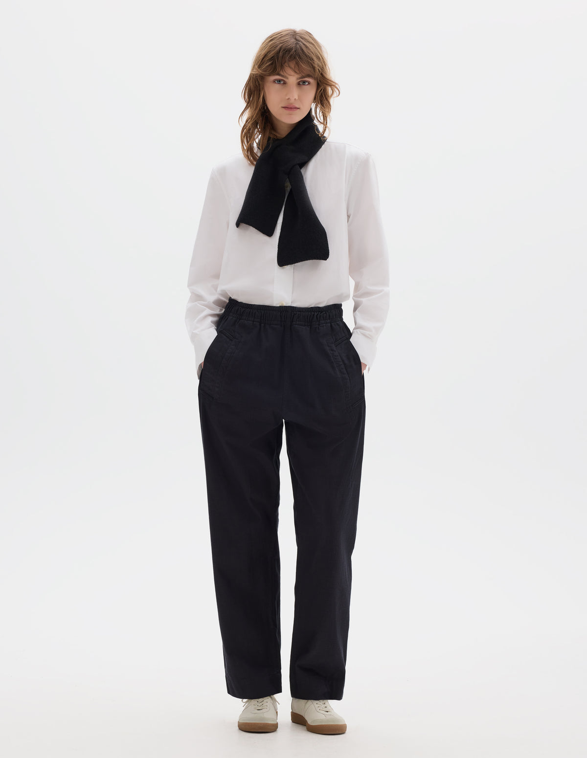 Full body image, front view of model wearing a dark blue relaxed wide leg joggers with elasticated waist and deep welt side pockets. Styled with a white shirt, black knitted scarf and off white suede trainers.