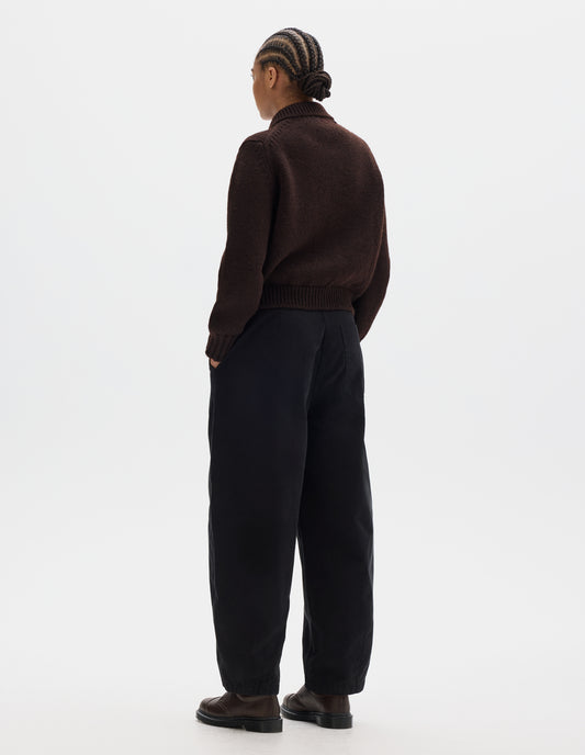 Full body image, back view of model wearing a dark brown boxy fit collared cardigan, rib detailing on collar, hem and cuffs. Styled with black trousers, brown leather shoes.