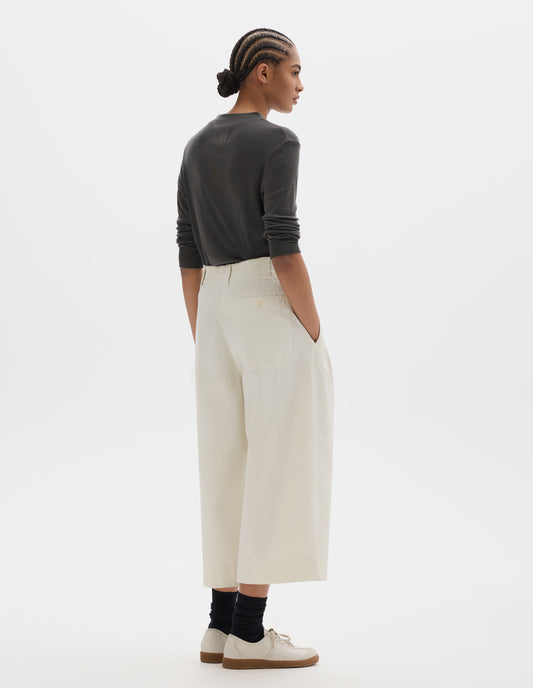Full body image, back view of model wearing a greyish jersey wool top, off white wide leg culotte trousers. Styled with black socks and beige trainers.