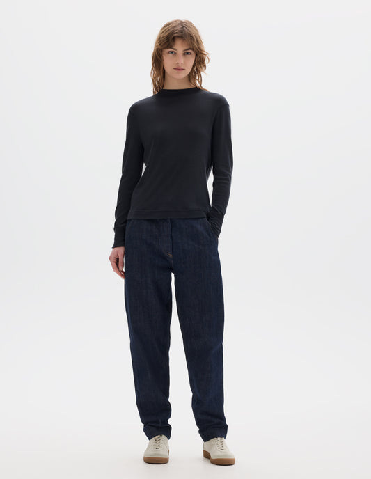 Full body image, front view of model wearing black long sleeve t shirt with set-in sleeves, a rib neck and cuffs with flatlock stitching. Styled with indigo denim jeans and white trainers with gum sole. 