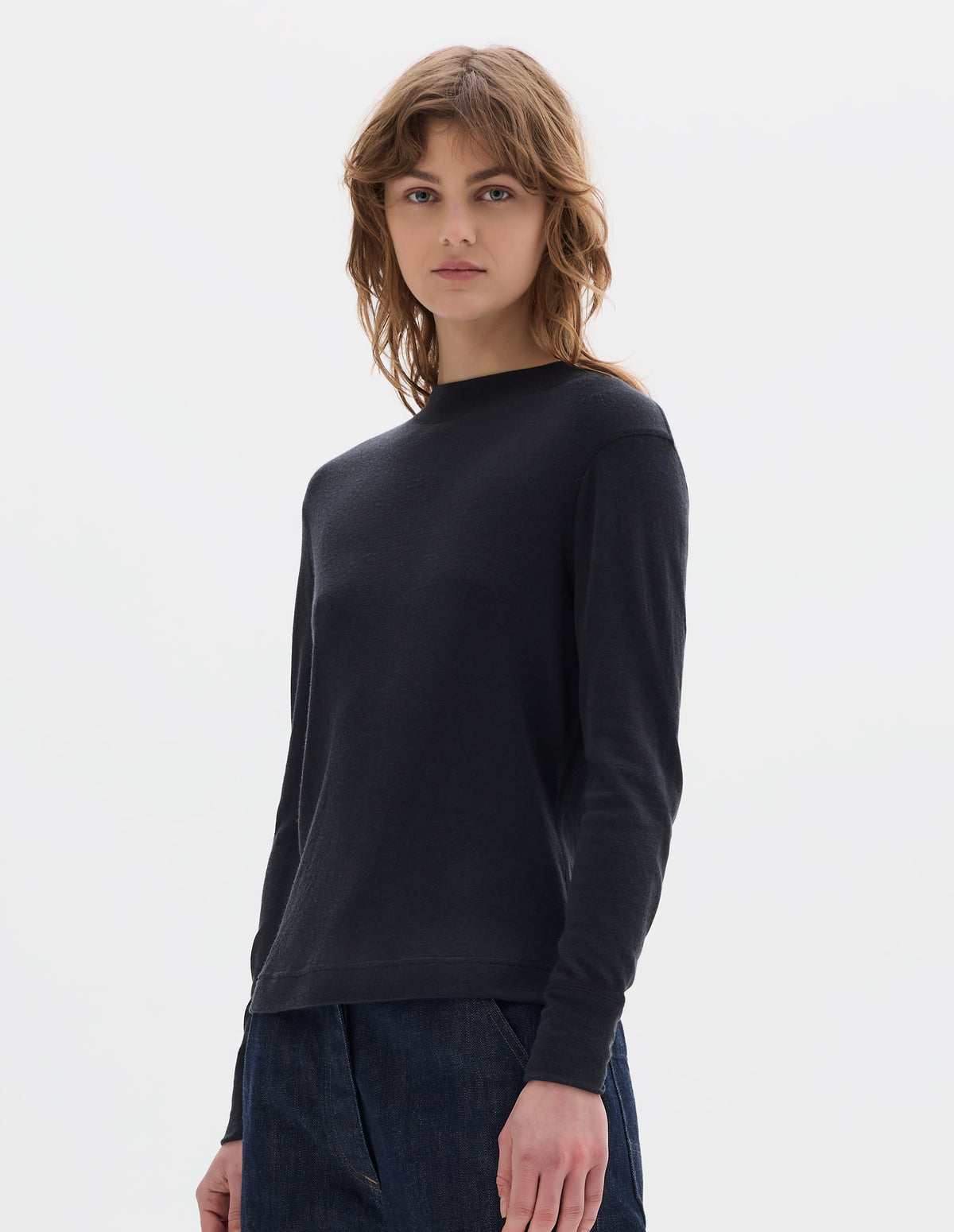 Cropped body image, front view of model wearing black long sleeve t shirt with set-in sleeves, a rib neck and cuffs with flatlock stitching. Styled with indigo denim jeans.