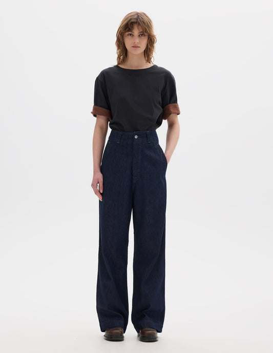Full body image, front view of model wearing indigo blue wide leg light denim twill jeans. With metal button closure, button through waistband and slant side pockets. Styled with black short sleeve t shirt with faced cuffs with a contrast brown on the reverse and brown leather shoes.