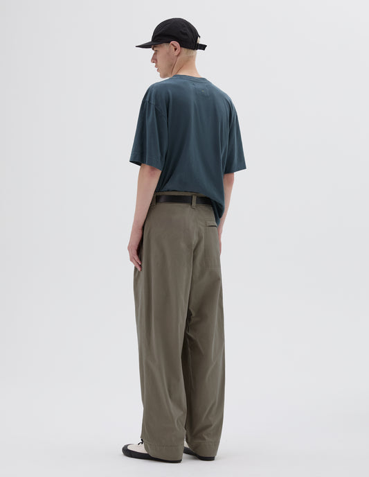 Full body image, back view of model wearing light green double pleated trousers with zip fly back pocket. Styled with blue cotton t-shirt, black leather belt, white canvas trainers and black cap.
