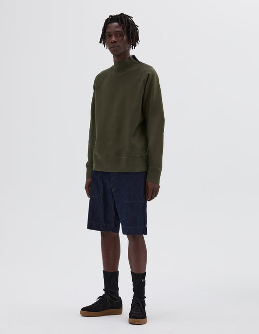 Full body image, front view of model wearing green zip neck sweatshirt, styled with denim shorts, black socks and black nubuck trainers.