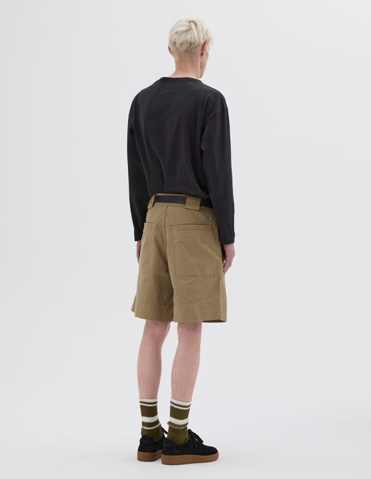 Full body image, back view of model wearing beige shorts with slant pockets, belt loops and deep stitch hem. Styled with black long sleeve smock neck t-shirt, black leather belt, green and white striped socks and black nubuck trainers.