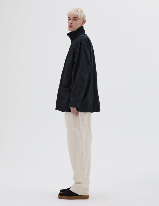 Full body image, side view of model wearing dark navy jacket with contrast ribbed collar and press stud fastening welt pockets. Styled with off white trousers and black nubuck trainers. 