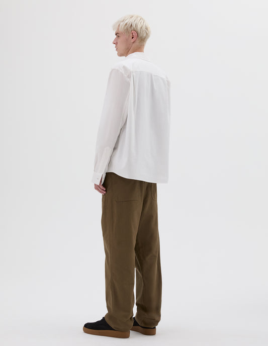 Full body image, back view of model wearing green relaxed cut trousers, with patch back pockets and deep stitch hem. Styled with white long sleeve shirt and black nubuck trainers.