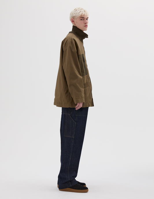 Full body image, side view of model wearing green jacket with contrast ribbed collar and contrast zip chest pocket. Styled with denim trousers and black nubuck trainers. 