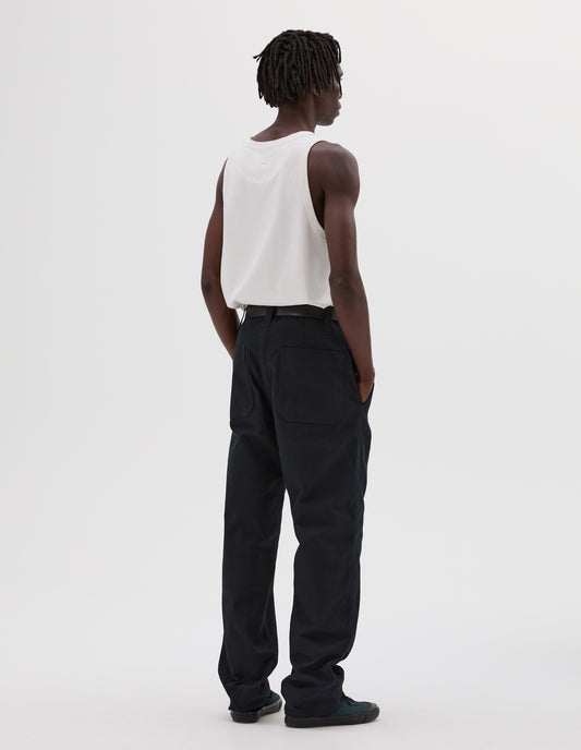 Full body image, back view of model wearing dark navy relaxed cut trousers, with dropped belt loops, patch back pockets and deep stitch hem. Styled with white cotton vest, black leather belt and green canvas high top trainers.
