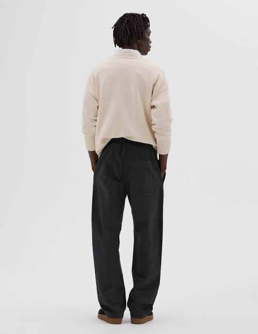 Full body image, back view of model wearing charcoal grey wide leg trousers, with elasticated waist and  patch back pocket. Styled with white shirt, cream ribbed jumper and black nubuck trainers.