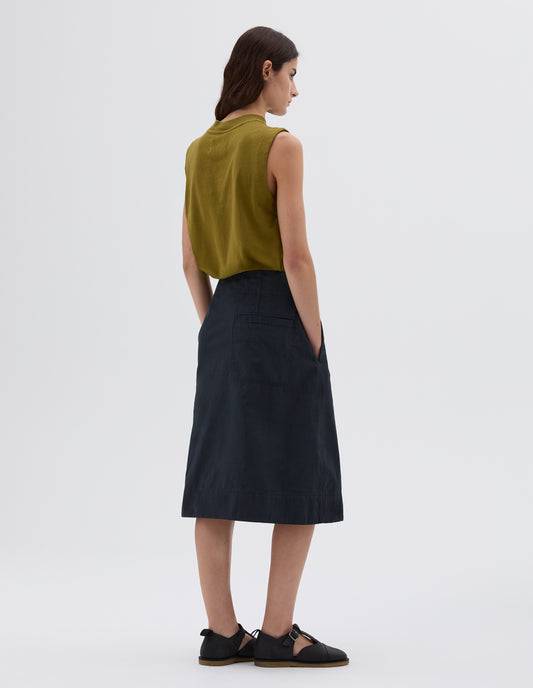 Full body image, back view of model wearing blue midi length welt back pocket, styled with green sleeveless top and black leather sandals.