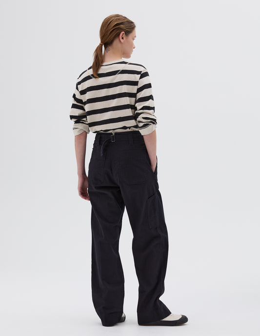 Full body image, back view of model wearing dark blue relaxed straight leg trousers with cinch back and belt loops, back pockets, side pockets and tool pocket on right leg, styled with black and beige stripy long sleeved t-shirt with white and black trainers.