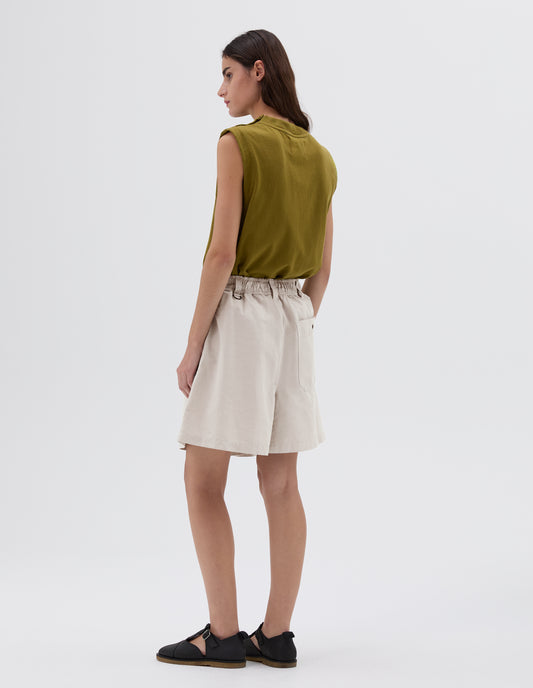 Full body image, back view of model wearing light grey relaxed shorts with press stud fastening on back pocket and three belt loops with one D-ring detail, styled with green sleeveless top and black leather sandals.