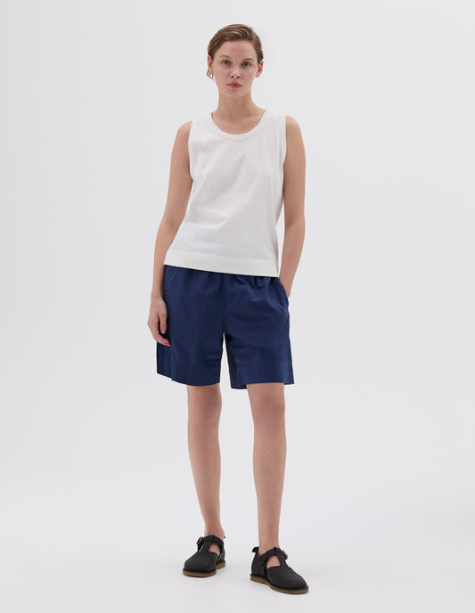 Full body image, front view of model wearing white regular cut vest, styled with blue shorts and black leather sandals.
