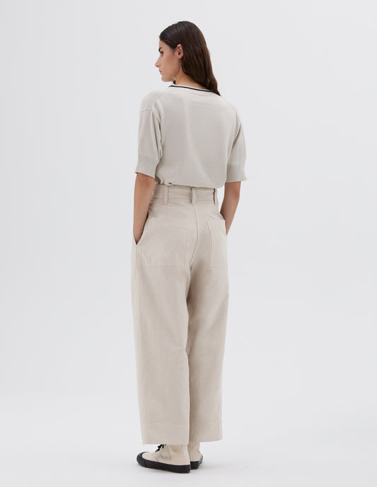 Full body image, back view of model wearing light grey wide leg cropped trousers with side and back pockets and belt loops, styled with beige knitted t-shirt and white and black high top trainers.