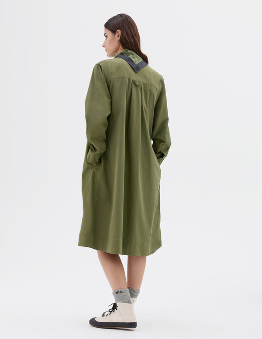 Full body image, back view of model wearing green midi length collarless swing dress with long sleeves, side pockets and hanger loop detail on back, styled with black and green scout scarf, light grey socks and white and black high top trainers. 