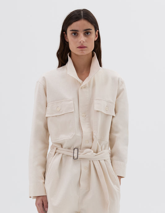 Cropped body image, front view of model wearing  relaxed white overalls with  button-through collar, slider buckle belt, corozo brace button fastening  and  button-through flap patch pockets, and side pockets.
