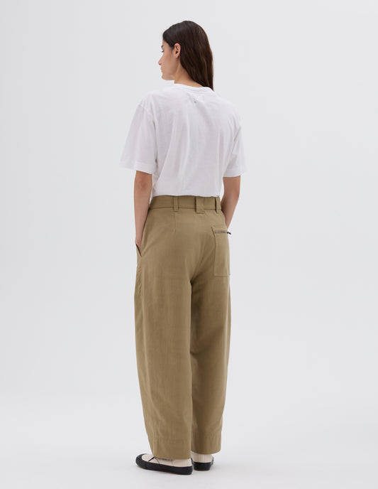 Full body image, back view of model wearing beige straight cut ankle crop trousers with side pockets, zip patch back pocket and belt loops, styled with white t-shirt and white and black trainers.
