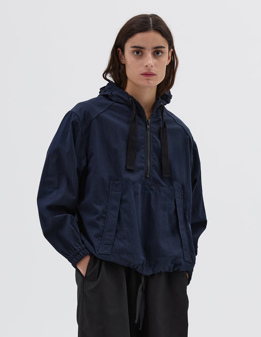 Cropped view of model wearing a navy blue drawcord hooded jacket, with kangaroo pocket and half zip fastening. Styled with black dress.