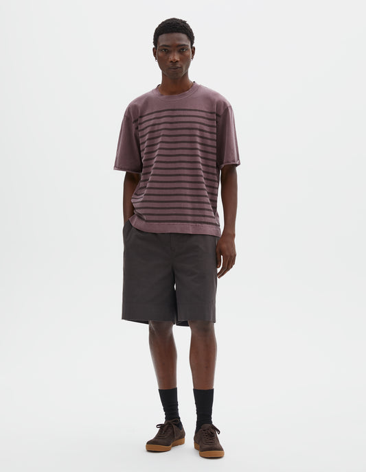 Full body image, front view of model wearing purple short sleeve cotton t-shirt with brown stripes, flatlock stitch seam detailing and rolled raw sleeve hems held with a single bar tack. Styled with dark brown shorts, black socks and brown suede trainers with gum sole.  