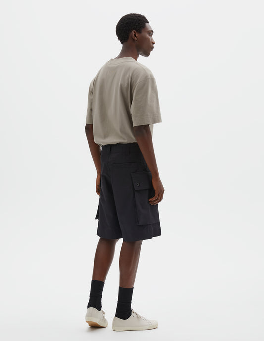 Full body image, back view of model wearing black cotton shorts with cargo pockets, belt loops and welt back pocket. Styled with beige t-shirt, black socks and off white canvas trainers. 
