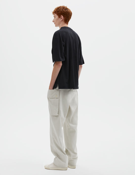 Full body image, back view of model wearing boxy black t-shirt with vent split hem. Styled with off white trousers and beige canvas trainers.