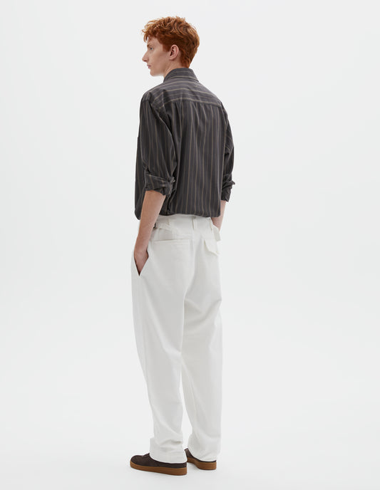 Full body image, back view of model wearing white cotton drill trousers with belt loops, side adjustors, welt back and flap back pockets. Styled with grey, black and green striped shirt and brown suede trainers.