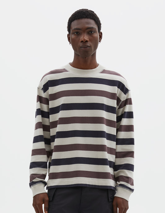 Cropped body image, front view of model wearing off white, dark navy and purple striped long sleeve top, with contrast rib on neckline and cuffs and flatlock stitch detailing. Styled with black shorts.