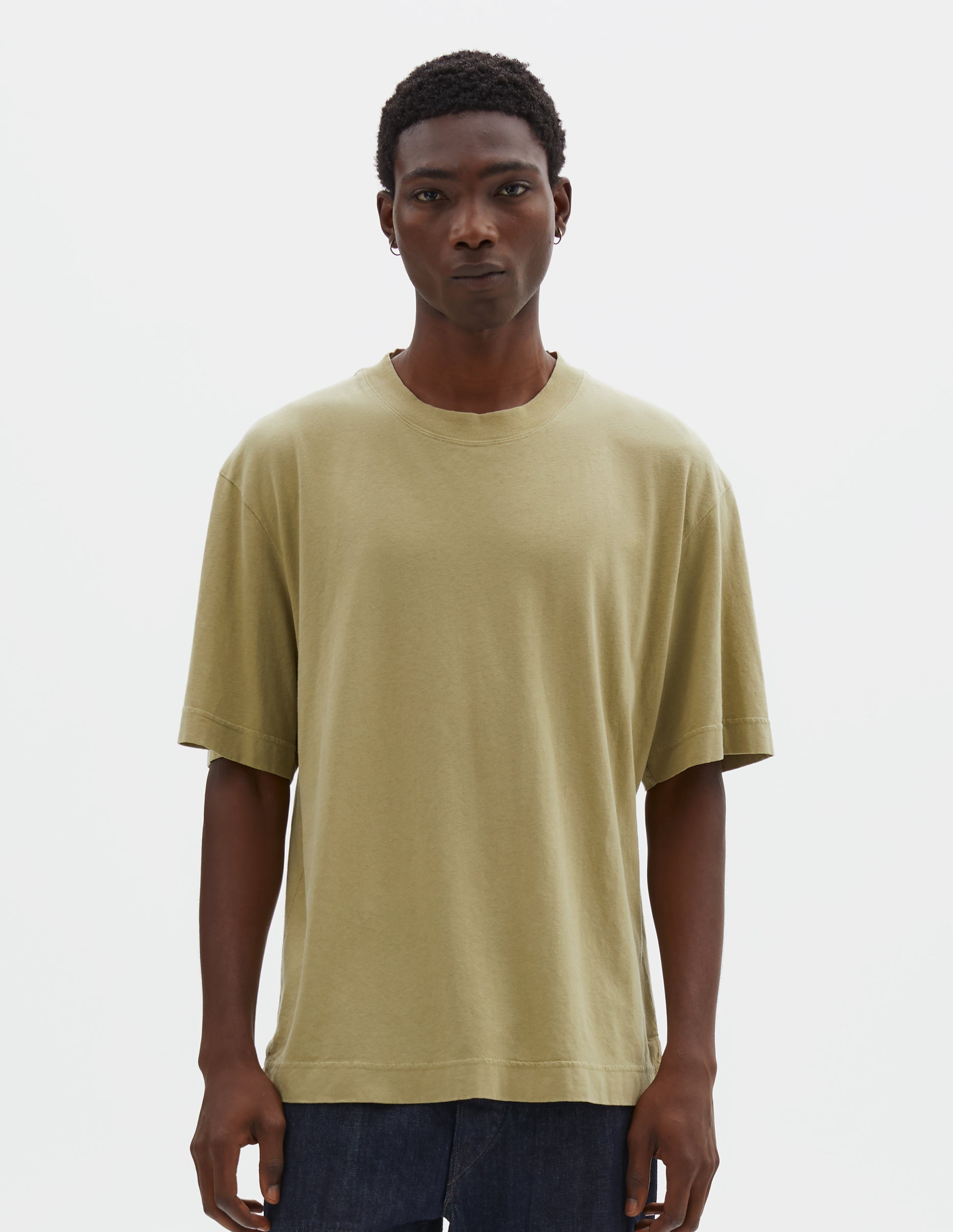 Cropped body image, front view of model wearing pale green cotton linen short sleeve t-shirt with vent split hem. Styled with indigo blue jeans.