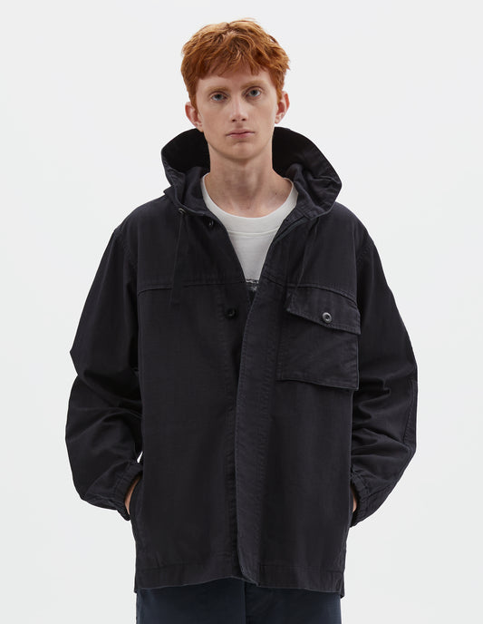 Cropped body image, front view of model wearing indigo blue twill hooded jacket, with flap patch chest pocket, concealed placket, drawcord adjustable hood and elasticated cuffs. Styled over white graphic t-shirt, with navy blue shorts.