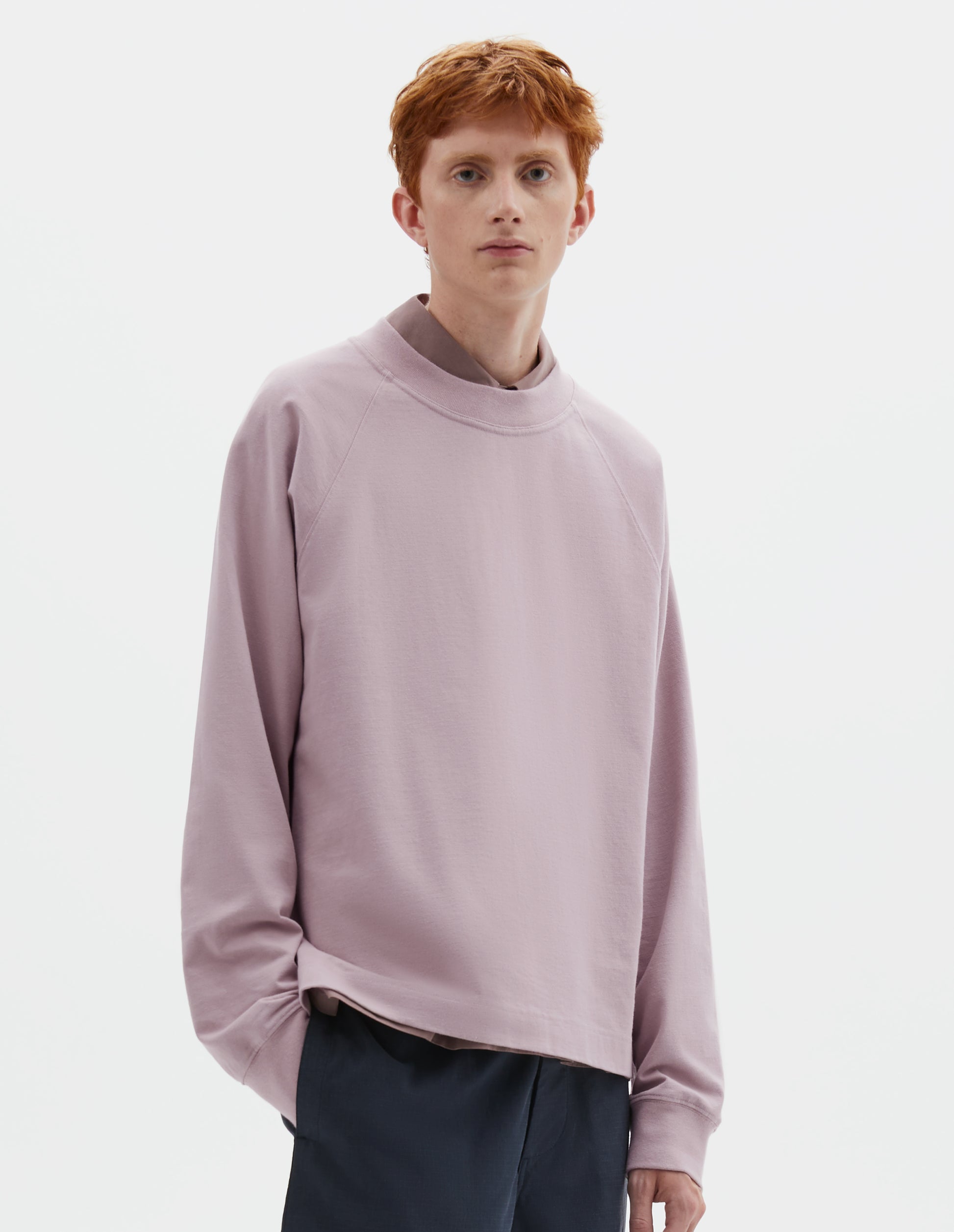 Cropped body image, front view of model wearing pink cotton long sleeve t-shirt with raglan sleeve and single rib trims on neck and cuffs. Styled over dark pink shirt and dark blue shorts.