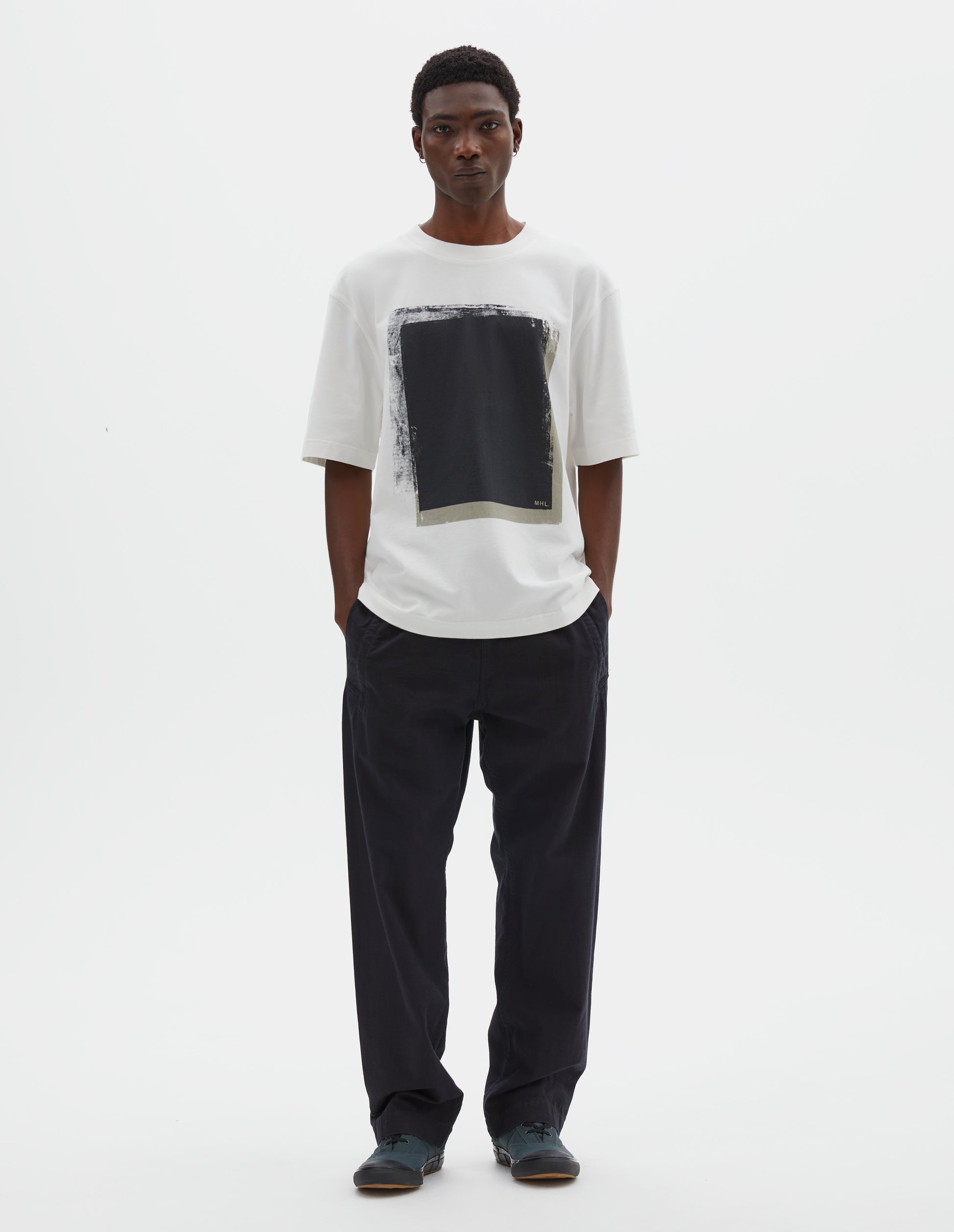 Full body image, front view of model wearing relaxed  wide leg black joggers with elasticated waist and deep welt pockets. Styled with white t-shirt and dark grey trainers.