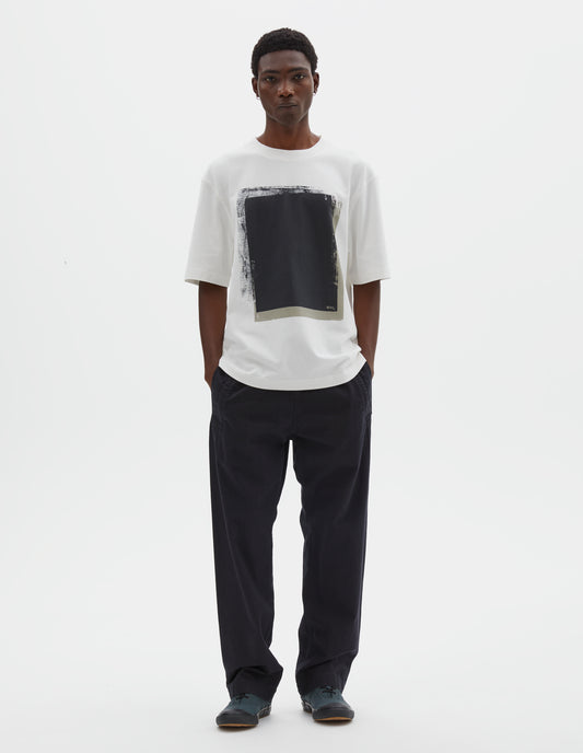 Full body image, front view of model wearing relaxed  wide leg black joggers with elasticated waist and deep welt pockets. Styled with white t-shirt and dark grey trainers.