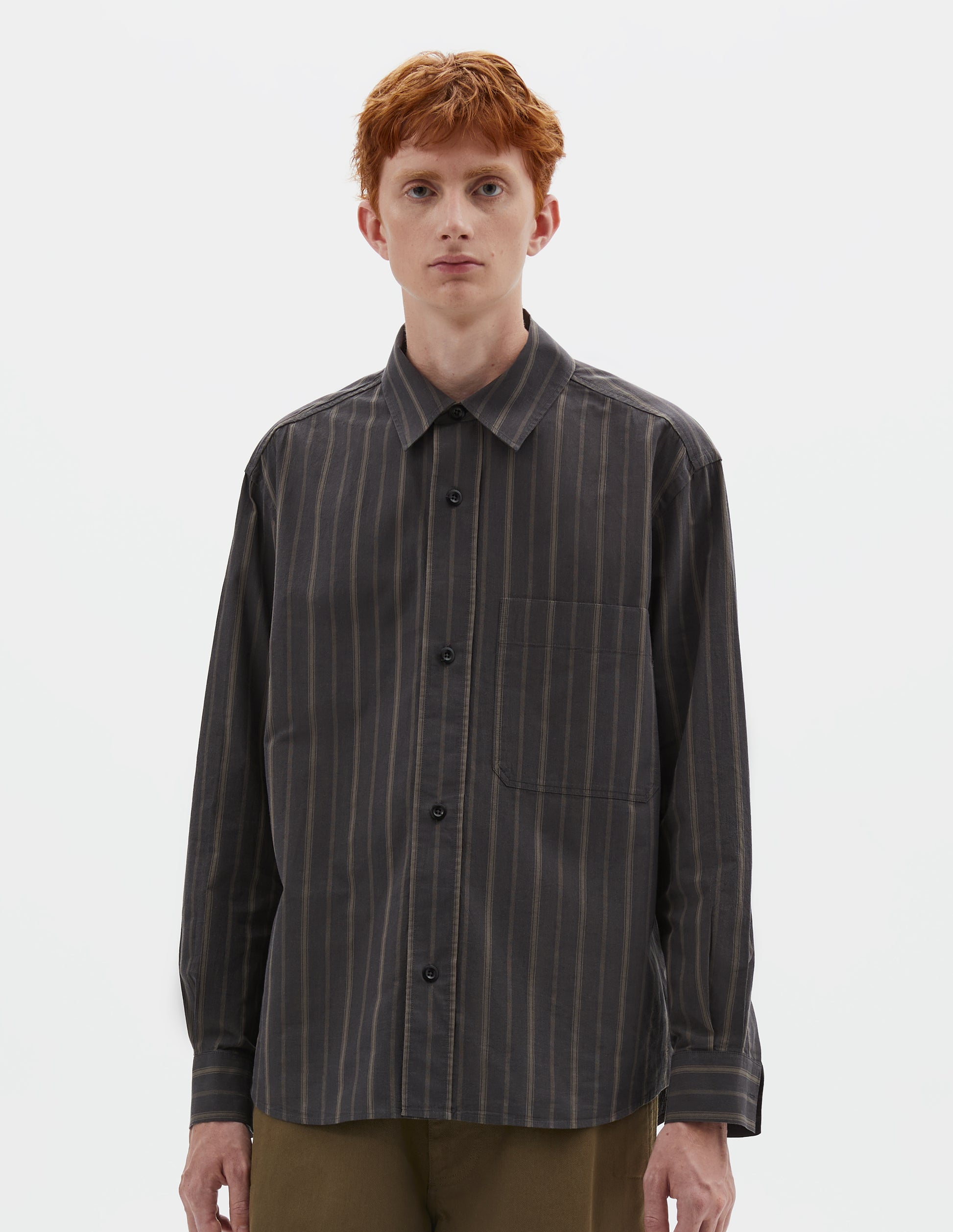 Cropped body image, front view of model wearing off black and khaki striped shirt, with corozo button fastening and patch chest pockets. Styled with khaki green trousers.