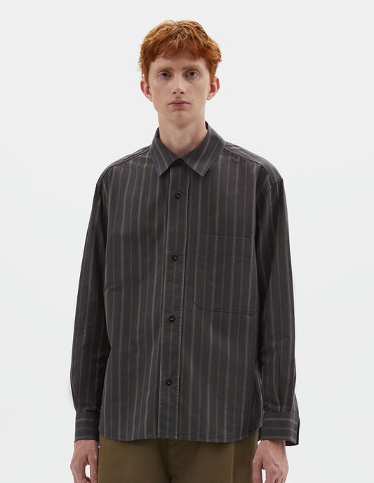 Cropped body image, front view of model wearing off black and khaki striped shirt, with corozo button fastening and patch chest pockets. Styled with khaki green trousers.