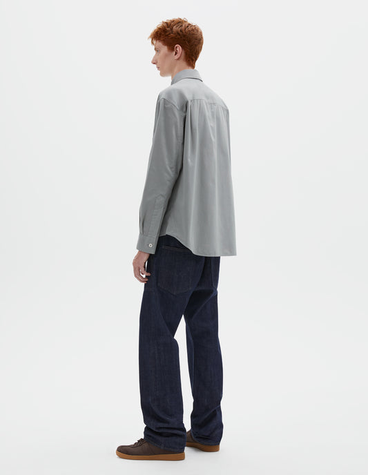 Full body image, front view of model wearing indigo denim twill jeans, with metal button fly, grown on waistband with belt loops and back pockets with half cotton lining. Styled with grey shirt and brown suede trainers.