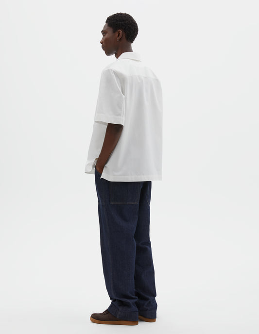 Full body image, back view of model wearing indigo blue denim twill jeans. With metal button tab waist adjusters, belt loops and patch and hammer pocket on back of trousers. Styled with white shirt and brown suede trainers.