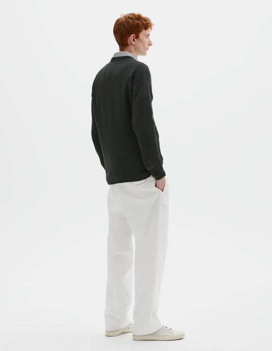 Full body image, back view of model wearing dark grey merino wool sweatshirt with raglan sleeve and contrast rib on neck, cuffs and hem. Styled over grey shirt, with white trousers and beige canvas trainers.