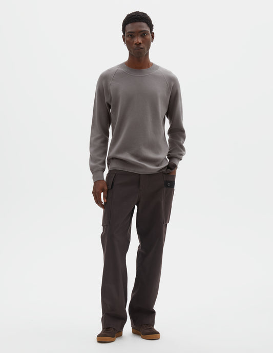 Full body image, front view of model wearing light grey merino wool sweatshirt with raglan sleeve and contrast rib on neck, cuffs and hem. Styled with reddish brown trousers and brown suede trainers.
