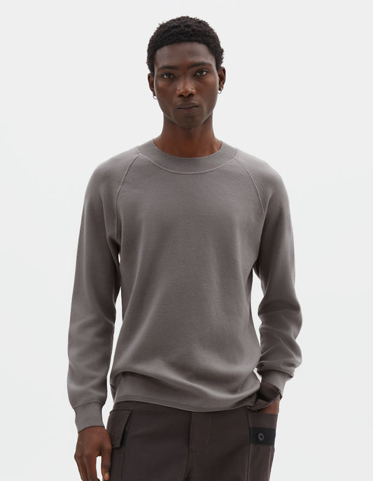 Cropped body image, front view of model wearing light grey merino wool sweatshirt with raglan sleeve and contrast rib on neck, cuffs and hem. Styled with reddish brown trousers.