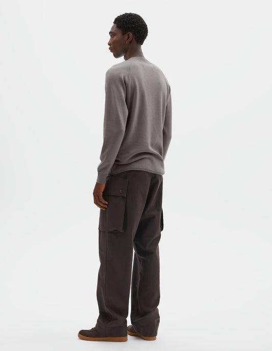 Full body image, back view of model wearing light grey merino wool sweatshirt with raglan sleeve and contrast rib on neck, cuffs and hem. Styled with reddish brown trousers and brown suede trainers.