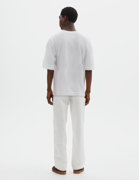 Full body image, back view of model wearing boxy white t-shirt with vent split hem. Styled with off white trousers and brown suede trainers.