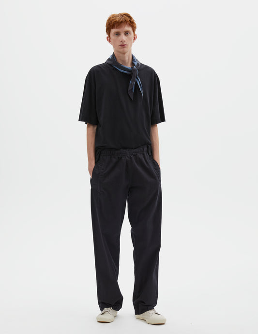 Full body image, front view of model wearing relaxed dark blue joggers with elasticated waist and deep welt pockets. Styled with navy blue t-shirt, blue and navy cotton scout scarf and beige canvas trainers.