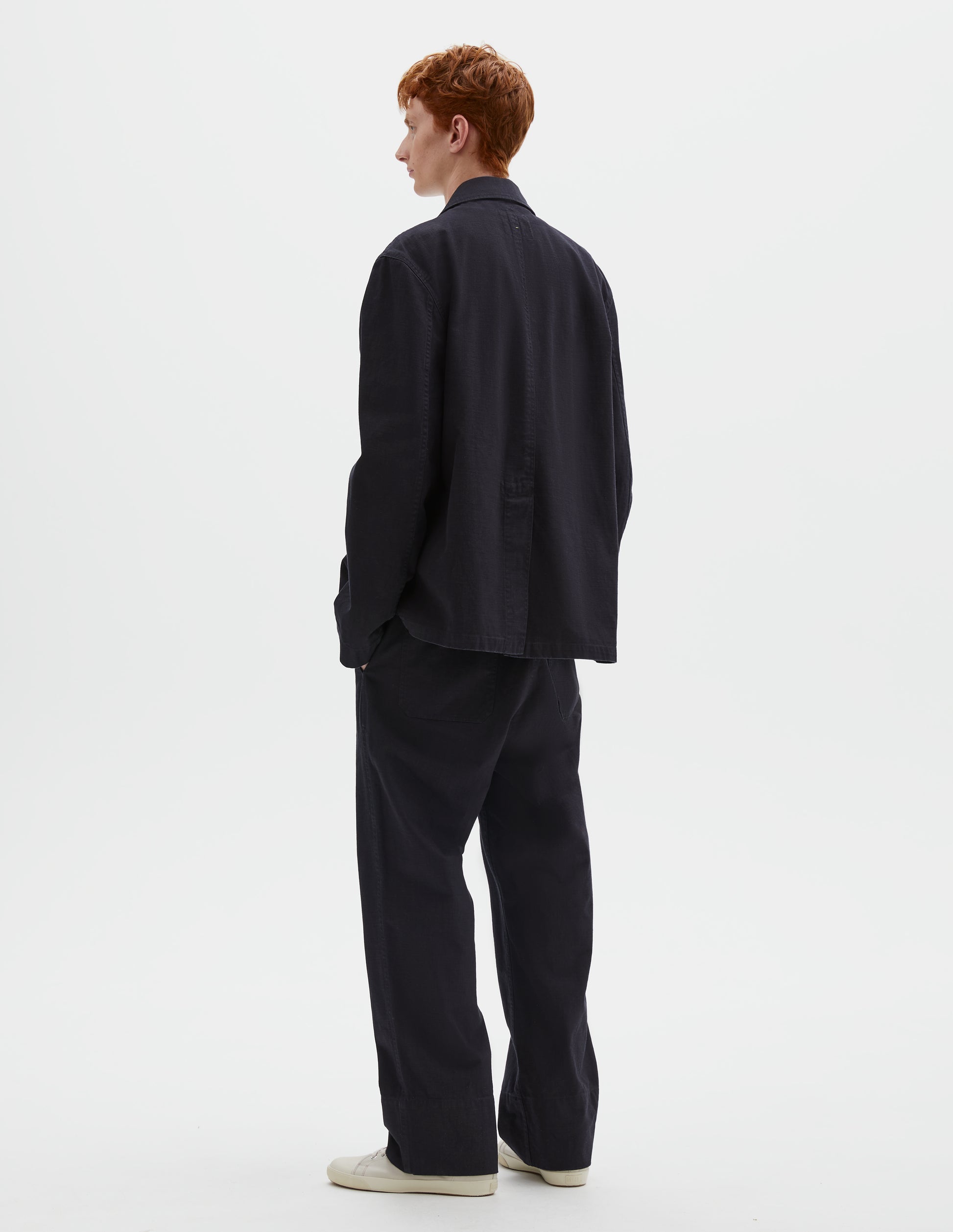 Full body image, back view of model wearing indigo blue twill blazer with back centre vent. Styled with matching indigo blue twill trousers and beige canvas trainers.