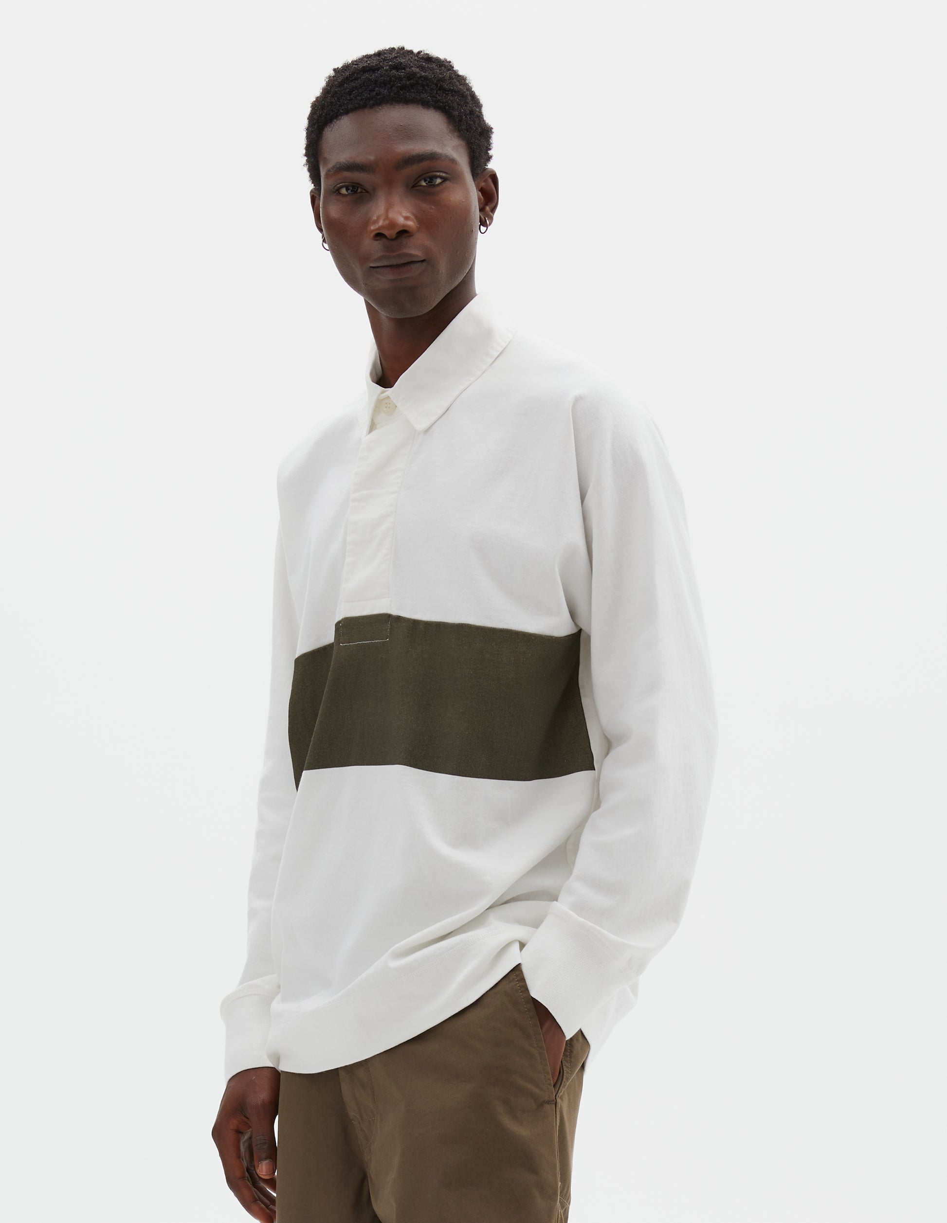 Cropped body image, front view of model wearing off white rugby long sleeve polo shirt with dark green panel across chest, twill collar, wide fly front placket and rib cuffs. Styled with green trousers.